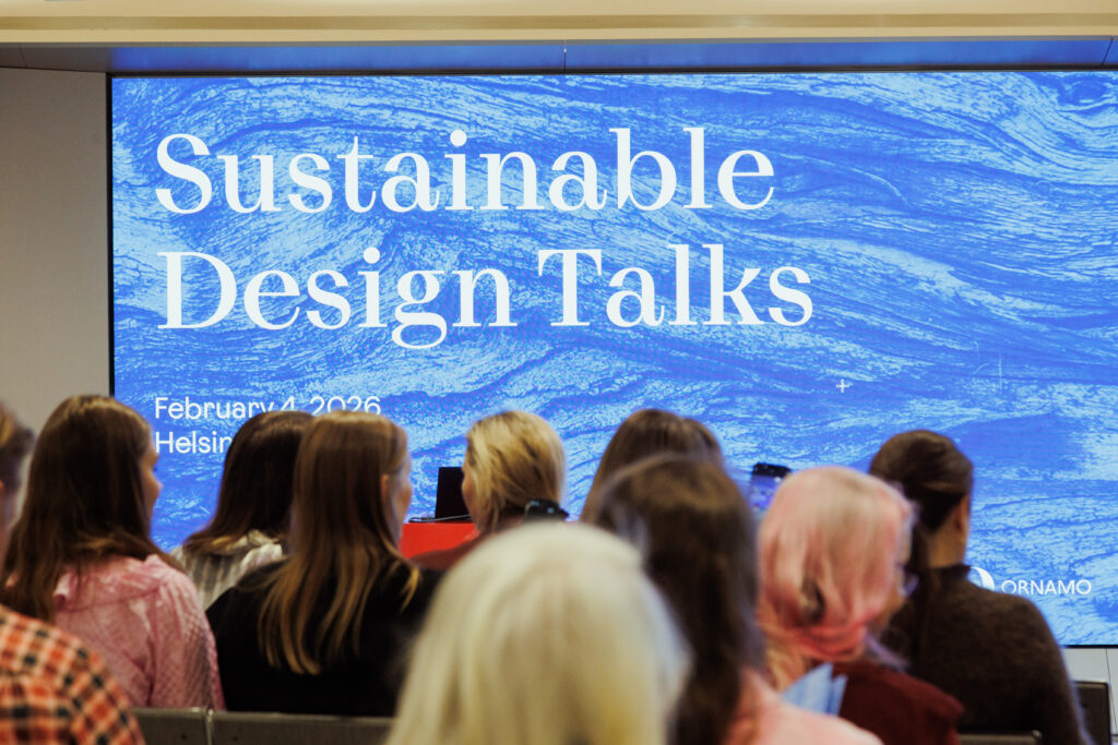 Audience gathered at Sustainable Design Talks, facing a large screen displaying the event title in a bright blue visual backdrop at Helsinki City Hall.