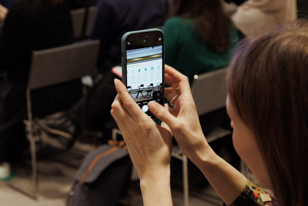 Close-up of an attendee taking a photo of a presentation slide outlining essential sustainability skills for designers.